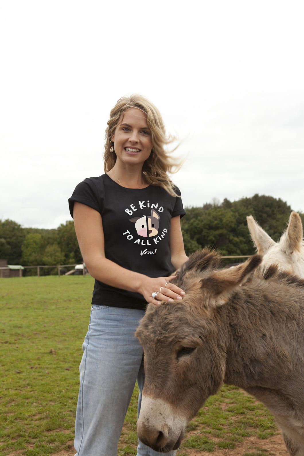 Woman wearing a 'Be Kind to All Mammals' t-shirt petting a donkey in an outdoor setting.
