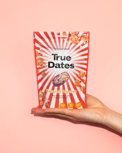 A hand presents a red-and-white striped pouch of True Dates Caramel Popcorn against a soft pink background, creating a bright, playful snack-ad feel.
