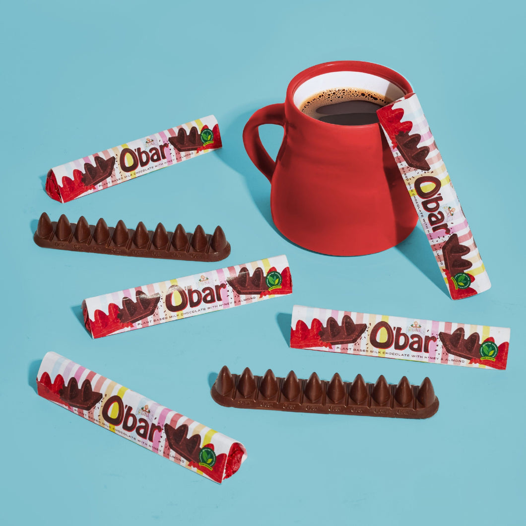 Five Obar chocolate bars with their paper wrappers are arranged around a red ceramic mug filled with dark coffee on a light blue background.