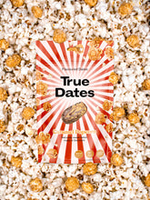 A packet of True Dates caramel popcorn lies on white popcorn and caramel-coated snacks, with bold red-and-white rays and a playful, indulgent look.