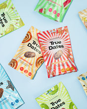Colourful True Dates snack packages arranged on a pale blue background, featuring date varieties like Caramel Popcorn, Cinnamon Roll, and watermelon; the playful, bright design feels cheerful and lively.