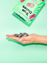 A hand holds several dark, sugar-dusted date candies beneath a tilted green-and-white striped snack package, creating a bright, playful product display.