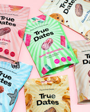 Colourful True Dates snack packages are scattered on a pink background, with a green Sour Watermelon pack centered among peach, cookie, and other flavors, creating a playful, bright tone.