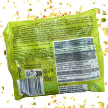 Back of a bright green Kookie Cat pistachio cookie package, showing ingredients, nutrition facts, barcode, and recycling symbols, with scattered crumbs on white.