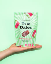 A hand holds a green-and-white “True Dates” pouch labeled “Sour Watermelon,” with date fruit and watermelon graphics, against a mint-green background. The scene feels bright and playful.