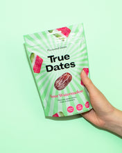A hand holds a green-and-white “True Dates” pouch labeled “Sour Watermelon,” with date fruit and watermelon graphics, against a mint-green background. The scene feels bright and playful.
